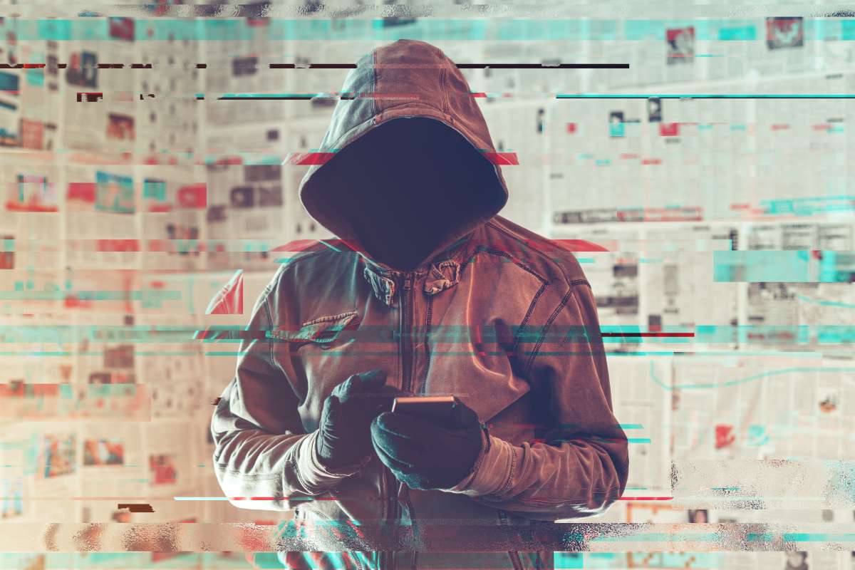 Hooded figure with shadowed face and gloves typing on a smartphone.